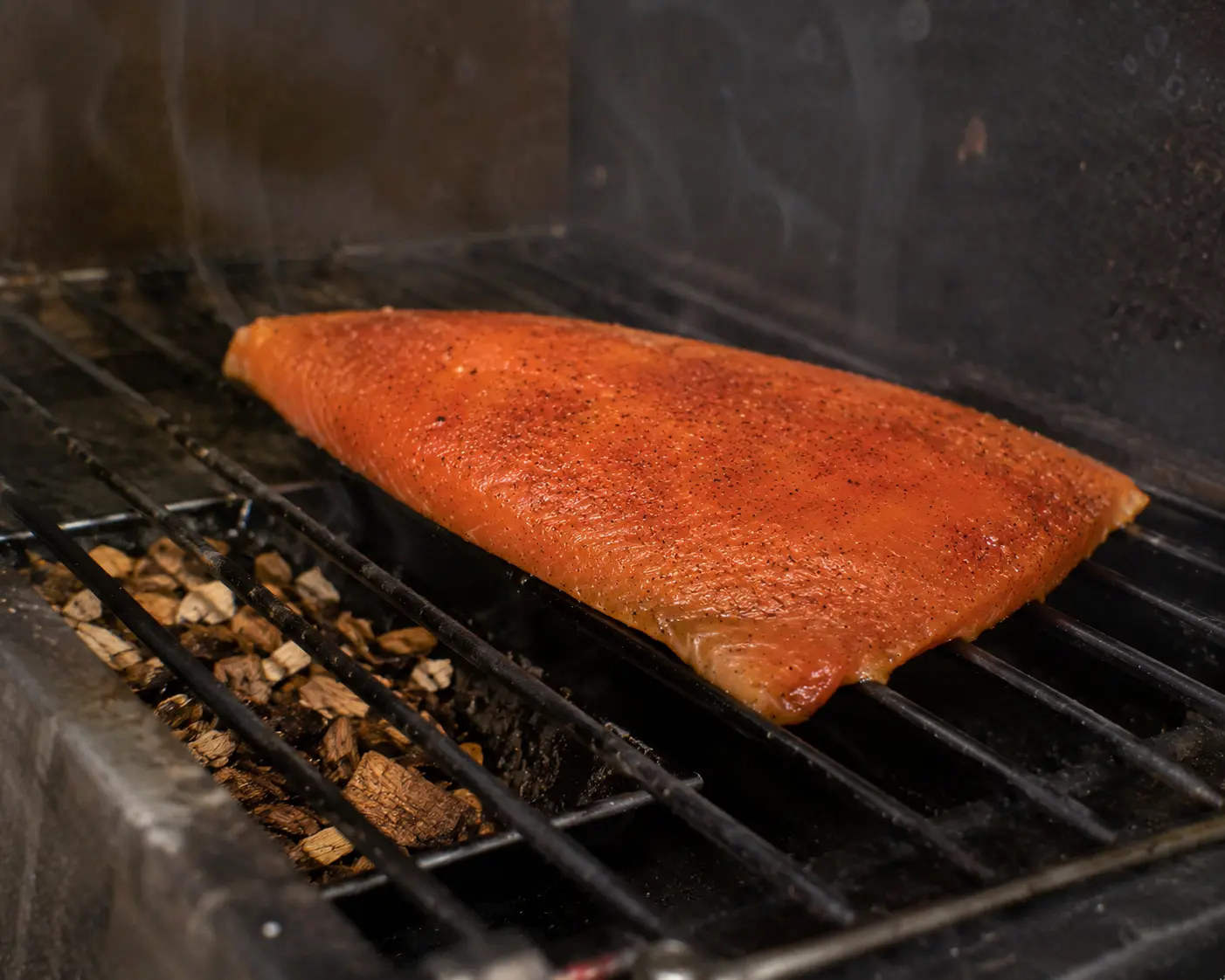 Filet de saumon sur la grille du fumoir avec de la fumée visible